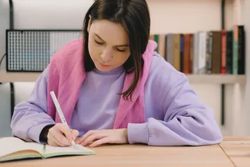 IELTS hazırlık programı: Kütüphanede masaya oturmuş, defterine not yazan öğrenci